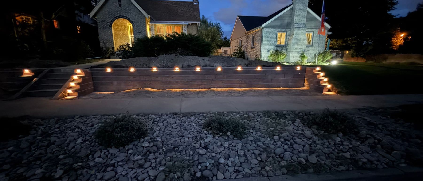 A long block retaining wall at dusk with a row of small lights along its face and steps.