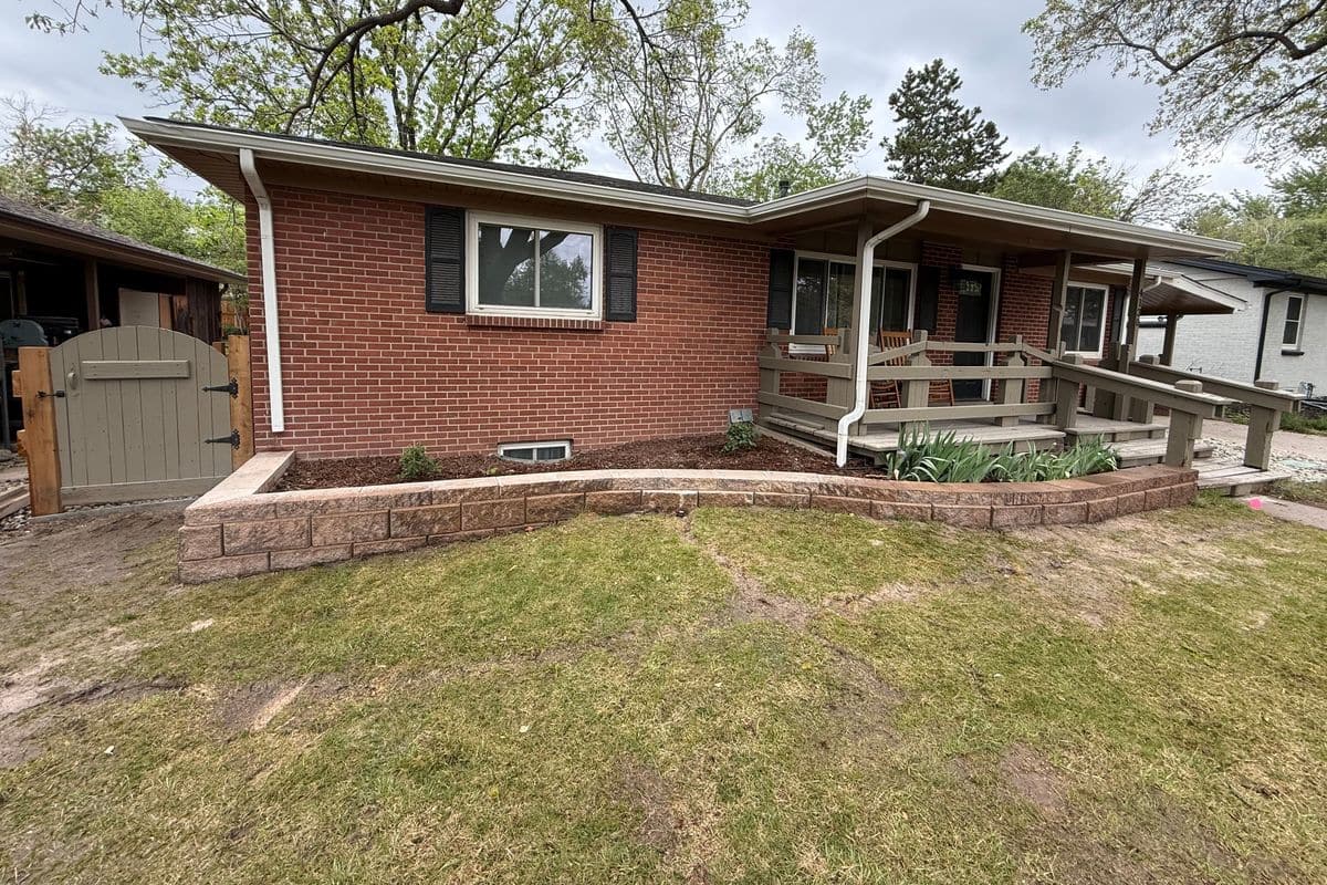 A low block retaining wall wrapping the front of a brick ranch home.